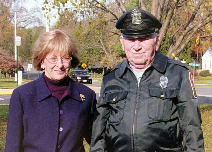 Color photograph of Principal Coose and Mr. Bill from our 2004 to 2005 yearbook. They are standing in front of our school with the neighborhood visible behind them. Mr. Bill is wearing his school crossing guard jacket and hat. 